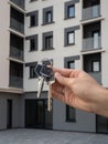 Female hand holding a set of three keys from a new apartment in a recently built house. Multi-storied building at backdrop in blur