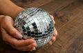 Female hand holding a shiny silver mirror disco ball on wooden background. Royalty Free Stock Photo