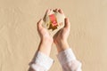 Female hand holding small heavenly isolation beach with deck chair, glass of juice, flip flops on handful of sand. Creative