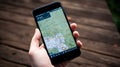 female hand holding a smartphone with a map on the screen on a wooden background Royalty Free Stock Photo