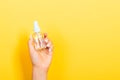 Female hand holding spray cream bottle of lotion isolated. Girl give cosmetic products on yellow background Royalty Free Stock Photo