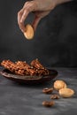 Female hand holding sweet cookie shaped nuts above waffle tubules with creamy and milk jam on grey cement background, food and Royalty Free Stock Photo