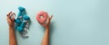 Female hand holding sweet donut, measuring tape, dumbbells over blue background. Top view, flat lay. Weight lost, sport, fitness, Royalty Free Stock Photo