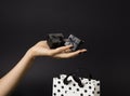 Female hand holding a three black gift-boxes on a palm, black gift-bag decorated with white polka dots below.