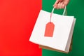 Female hand holding two shopping bags with price tag isolated on red and green background. Black friday sale, Christmas Royalty Free Stock Photo