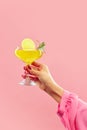 female hand holding vibrant citrus, tropical cocktail decorated with lemon slice and mint leaves against pastel pink Royalty Free Stock Photo