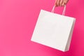 Female hand holding white blank shopping bag isolated on pink background. Black friday sale, discount, recycling