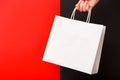 Female hand holding white blank shopping bag isolated on red and black background. Black friday sale, discount Royalty Free Stock Photo