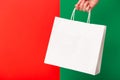 Female hand holding white blank shopping bag isolated on red and green background. Black friday sale, Christmas sale Royalty Free Stock Photo