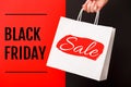 Female hand holding white shopping paper bag with Black Friday Sale text on red and black background. Sale, discount Royalty Free Stock Photo