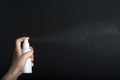 Female hand holding white sprey bottle and spray on dark background Royalty Free Stock Photo