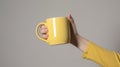 Female hand holding a yellow mug of unlabeled coffee.