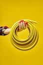 Female hand holding yellow Rubber Fuel Hose on Yellow Background, close-up.