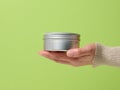 Female hand holds an aluminum jar for cream on a green background. Container for cosmetics