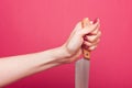 A female hand holds a clean knife with a wooden handle firmly and confidently on a pink blurred background. Royalty Free Stock Photo