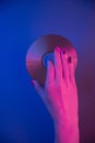 Female Hand Holds A Compact Disc On A Blue Background In Purple Neon Light.