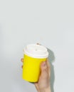 Female hand holds disposable yellow cardboard cup with coffee