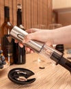 Female hand holds an electric corkscrew. And he opens a bottle of wine. In the background are bottles of wine, glasses and grapes Royalty Free Stock Photo