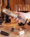 Female hand holds an electric corkscrew. And he opens a bottle of wine. In the background are bottles of wine, glasses and grapes Royalty Free Stock Photo