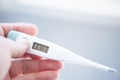 Female hand holds an electronic thermometer on a bokeh background.