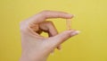 Female hand holds the fingers in capsule pill isolated on yellow background Royalty Free Stock Photo