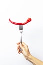 A female hand holds a fork with red chili pepper on white isolated background. Creative Food concept