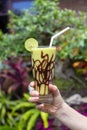 Female hand holds a fresh organic green smoothie from avocado, banana, cocoa and honey in glass . Close up