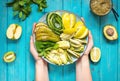 Female hand holds fresh salad with avocado, kiwi, apple, cucumber, pear, lime and mint with smoothie on blue wooden Royalty Free Stock Photo