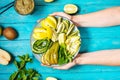 Female hand holds fresh salad with avocado, kiwi, apple, cucumber, pear, lime and mint with smoothie on blue wooden Royalty Free Stock Photo