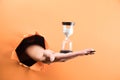 female hand holds hourglass on orange background