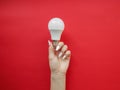 Female hand holds an LED lamp on a red background. Energy saving concept, alternative energy sources Royalty Free Stock Photo