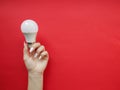Female hand holds an LED lamp on a red background. Energy saving concept, alternative energy sources Royalty Free Stock Photo