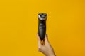 Female hand holds a male electric razor on a yellow background. Minimal style Royalty Free Stock Photo
