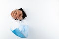 A female hand holds a medical mask through a hole in a white wall. Medical breakthrough concept, end of coronavirus