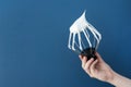 Female hand holds a metallic whisk with white protein cream on a blue background.