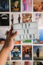 Female hand holds miniature cinema LED light box to wall with movie posters. Letters spell Top 10 Films. Royalty Free Stock Photo