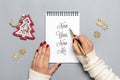 female hand holds pen and writes New Year, New Me on white notepad, tree, snowflake on gray background Top view Flat lay Business