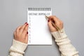 female hand holds pen, writing Christmas shopping list, gift ideas on white notepad on gray background Top view Flat lay Holiday Royalty Free Stock Photo