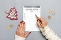 female hand holds pen, writing Christmas shopping list, gift ideas on white notepad on gray background Top view Flat lay Holiday Royalty Free Stock Photo