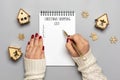 female hand holds pen, writing Christmas shopping list, gift ideas on white notepad on gray background Top view Flat lay Holiday Royalty Free Stock Photo