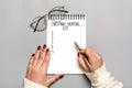 Female hand holds pen, writing Christmas shopping list, gift ideas on white notepad on gray background Top view Flat lay Holiday Royalty Free Stock Photo