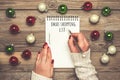 Female hand holds pen, writing Christmas shopping list, gift ideas on white notepad on wooden background Top view Flat lay Holiday Royalty Free Stock Photo