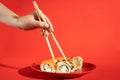 Female hand holds Philadelphia sushi roll with bamboo chopsticks on red background with hard shadow. Japanese food. Royalty Free Stock Photo