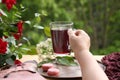 Female hand holds pomegranate, cherry juice, fruit drink in a glass mug, French pasta cake in the garden, clematis flowers, green Royalty Free Stock Photo