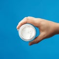 Female hand holds a round jar with white cream for face and body on a blue background Royalty Free Stock Photo