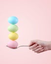 Female hand holds a spoon on which multi-colored eggs are balanced, on a pink background. Unusual design, Easter concept, copy