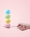 Female hand holds a spoon on which multi-colored eggs are balanced, on a pink background. Unusual design, Easter concept, copy