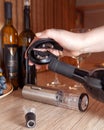 A female hand holds a stand for a corkscrew. Metal gray electric corkscrew and aerator lie on the table. In the background are