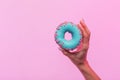 Female hand holds sweet blue donut with pink tasty small hearts on colored background. Close-up