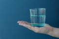 female hand holds transparent glass of water on blue background.